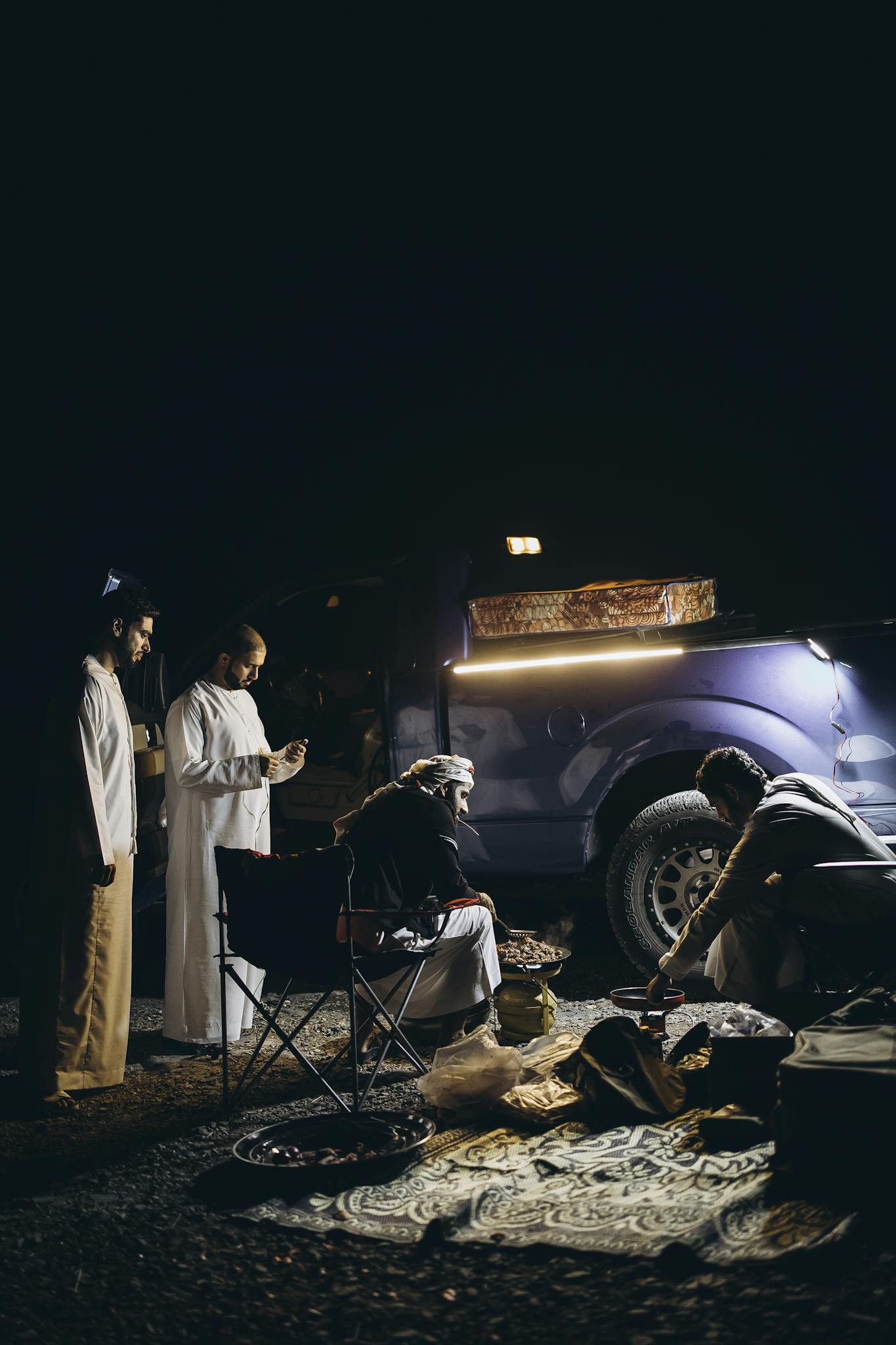 Group enjoying nighttime camping in Oman with off-road vehicle and tent under the starlit sky.