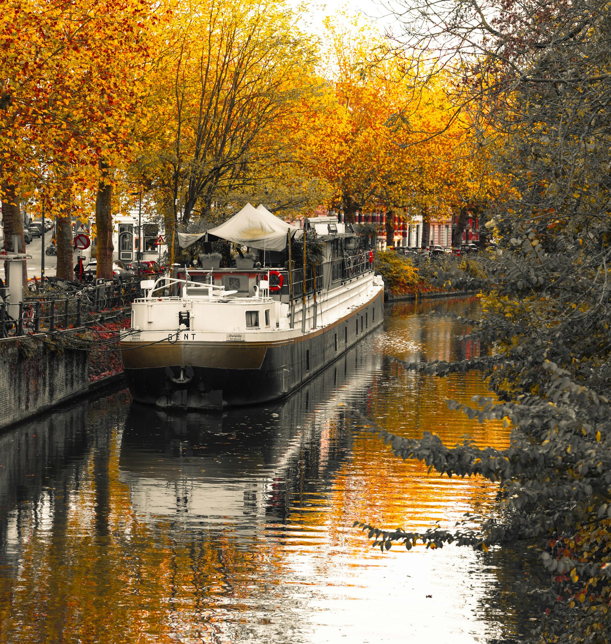 Serene autumn canal in Ghent with a boat reflecting vibrant fall colors.